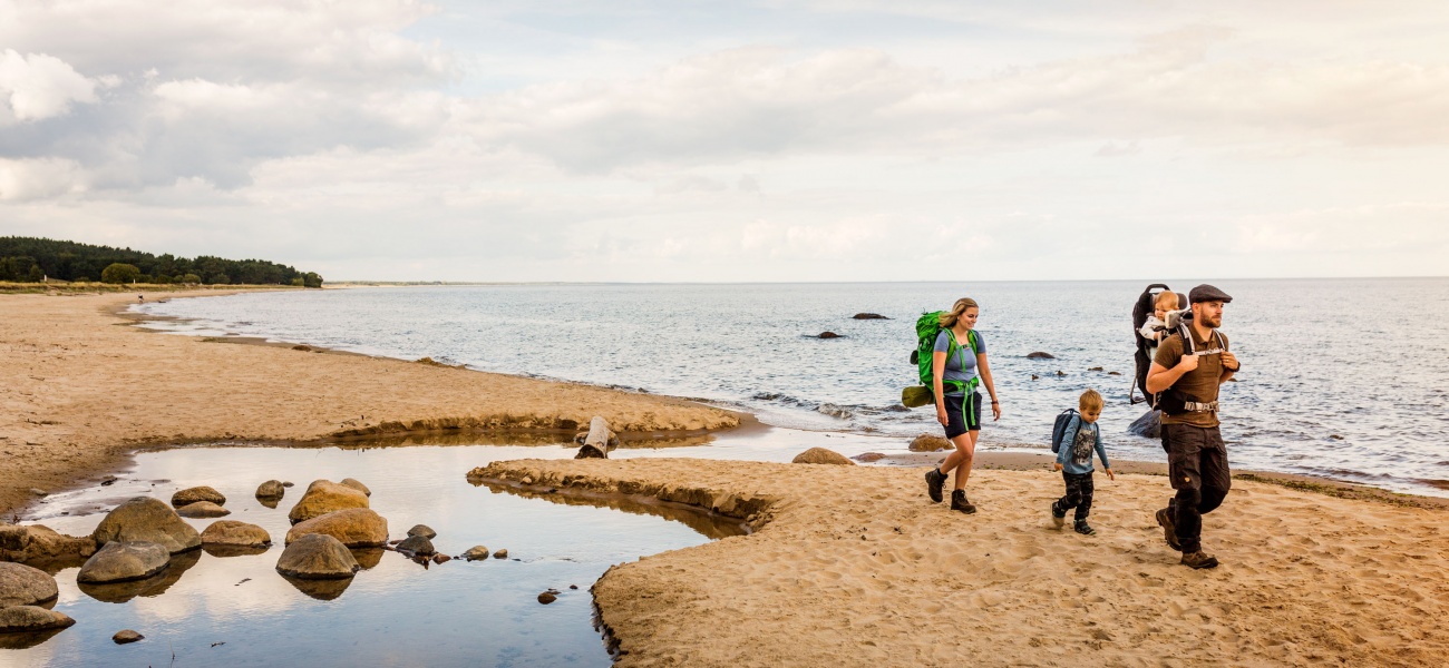 Three people walk across a beach in Skåne